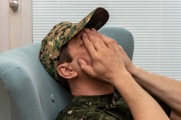An elderly man in a military uniform covered his face with his hands while sitting in an armchair. Concept: mental disorders in military personnel, treatment by a psychotherapist.