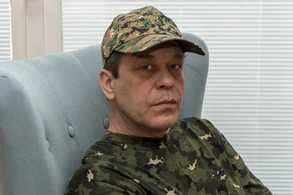 Psychologically depressed Elderly military man 45-50 years old in an army cap, sitting in a chair by the window. Concept: mental disorders in military personnel, treatment by a psychotherapist.