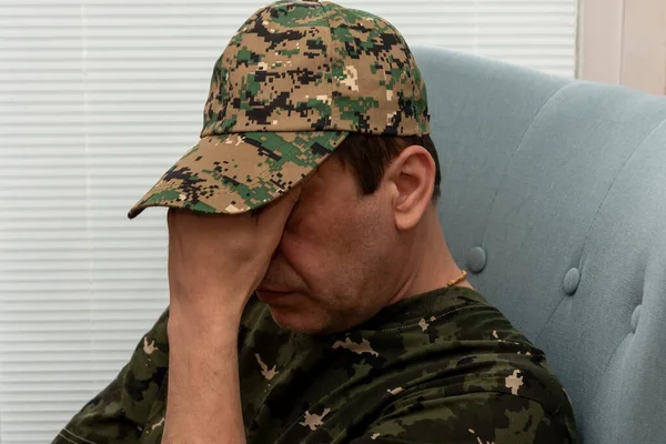 An elderly military man of 45-50 years covered his face with his hands while sitting in a chair. Concept: mental disorders in military personnel, treatment by a psychotherapist.