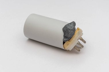 Arızalı, elektrikli motordan çıkan plastik kondansatör beyaz bir arka planda yırtılmış, izole edilmiş. Köpük şeklindeki iç bileşim, davanın kapağını yırttı ve dışarı çıktı..
