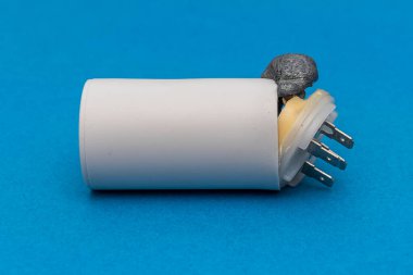 Faulty electric starting capacitor for electric motors on a blue background. The internal composition in the form of foam tore off the lid and came out. clipart