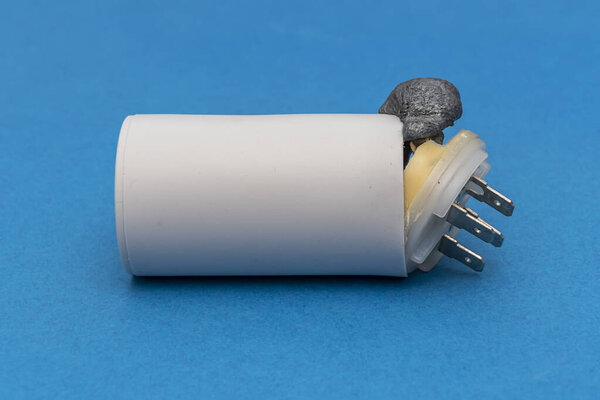 Faulty electric starting capacitor for electric motors on a blue background. The internal composition in the form of foam tore off the lid and came out.