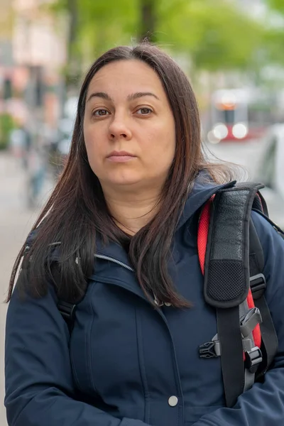 stock image An emotional portrait of a 40-45-year-old woman on a neutral blurred urban background with a backpack and a bag on her shoulders.