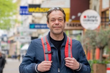 Şehrin bulanık arka planında yaşlı yakışıklı bir adam, omuzlarında bir turist çantası..