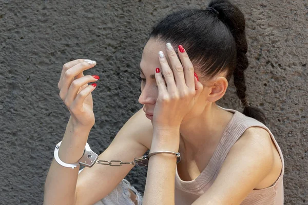 手錠をかけられた若い女性は灰色の背景に顔を隠す — ストック写真