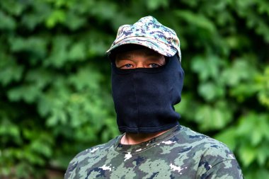 Yeşil ormanın bulanık arka planında kar maskesi ve kamuflajlı paralı asker.. 