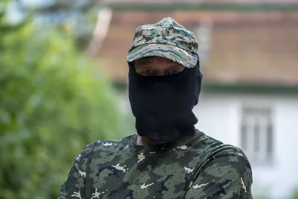 Military mercenary, balaclava hides his face, camouflage uniform, on a blurry background of city buildings. Concept: private military company, armed conflict, war in Ukraine.