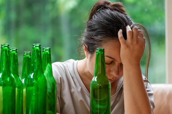 A grown woman sits at a table with beer bottles. Concept: female alcoholism, beer addiction, family quarrel.