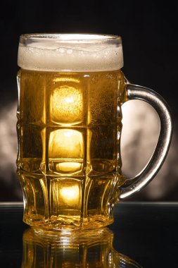 Koyu arka planda bira ve köpüklü cam bardak..