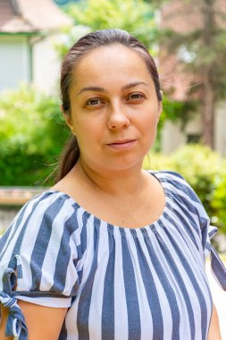 40-45 yaşlarında bir kadın doğanın arka planında ve evinde kameraya bakıyor..