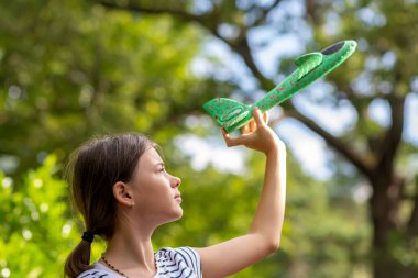 Yeşil bahçe ve gökyüzüne karşı oyuncak uçak fırlatan bir kız..