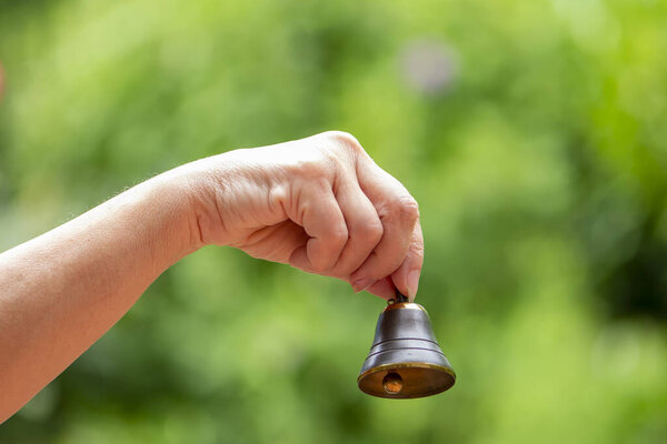 A small bell in the hand of an old woman on the background of nature, close-up, Concept: first bell, ringing bell, call or signal.