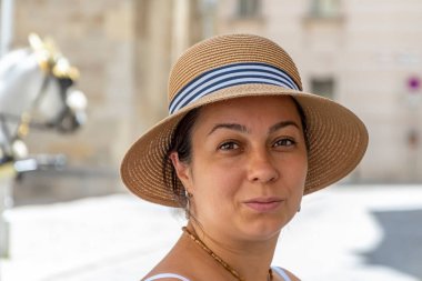 Hasır şapkalı gülümseyen orta yaşlı bir kadın bir Avrupa şehrinin arka planında, at arabasıyla.