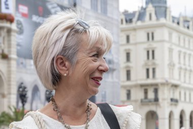 60-65 yaşlarında gülen yaşlı bir kadının duygusal portresi Avrupa 'nın tarafsız bir şehrinin arka planına karşı.