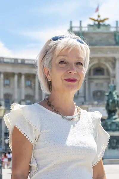 Portrait of a woman 60-65 years old in summer against a blurred background of ancient architecture of the Austrian city of Vienna, tourism and travel.