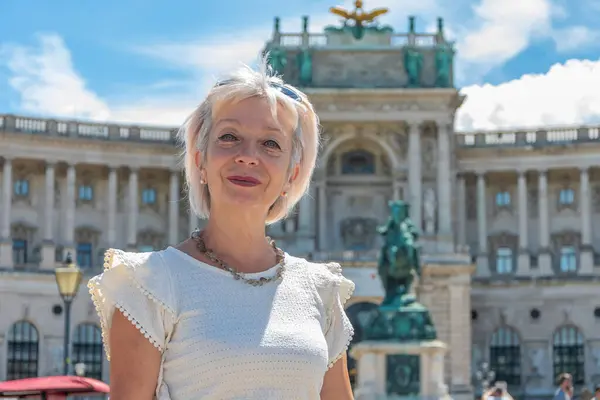 Portrait of a woman 60-65 years old in summer on the blurred background of the ancient architecture of the Austrian city of Vienna, tourism and travel.
