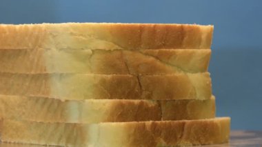 Dilimlenmiş beyaz ekmek yığını mavi arka planda dönüyor, tahta dilimleme tahtası, döngülü video.