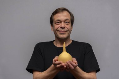 45-50 yaşlarında, elinde lavman olan yaşlı bir adamın portresi. Kavram: yaşlılıkta kabızlık, tedavi ve rahatlama.