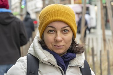 40-45 yaşlarında güzel bir kadın kameraya bakıyor, insanlar geçiyor, sokak portresi yapıyor..