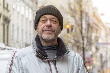 50-55 yaşlarında yaşlı ve gülümseyen sakallı bir adam Avrupa 'da bir şehrin arka planına karşı şapka takıyor..