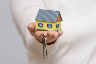 Bir kadının elinde küçük bir ev ve metal anahtarlar var..