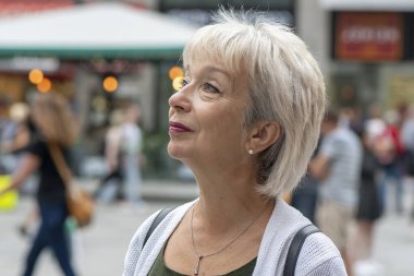 65-70 yaşlarında yaşlı gri saçlı bir kadın bulanık bir şehir geçmişine bakıyor..