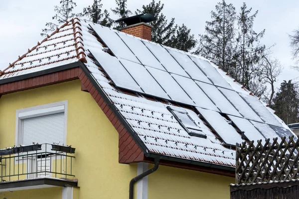 Solar panels on the tiled roof of a house covered in snow and ice, lack of electricity.