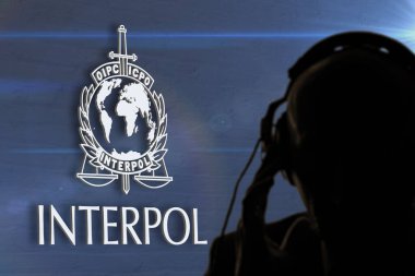 Interpol amblemine karşı kulaklık takan gizli ajanın silueti ve mavi desenli duvar, renkli gölgeler.