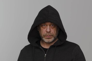 Gri sakallı, kapüşonlu, gri arka planda kapüşonlu yaşlı bir adamın portresi..