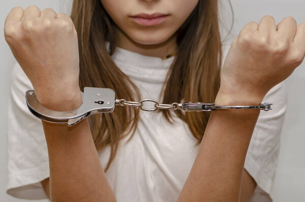 Подросток в наручниках на сером фоне. Несовершеннолетний преступник, уголовная ответственность несовершеннолетних. 
