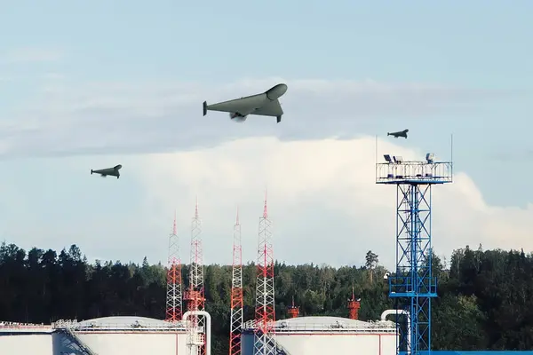 A group of military drones fly over oil refinery tanks, aerial attack.