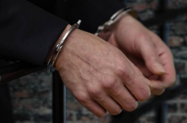 Kelepçeli bir adamın elleri bir hapishane hücresinin demir parmaklıklarında, özgürlüğüne bağlı..