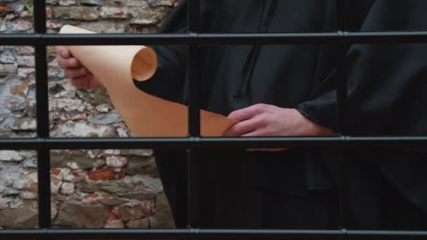 Μοναχός Πίσω Από Κάγκελα Ξεδιπλώνεται Και Διαβάζει Έναν Χάρτινο Πάπυρο — Αρχείο Βίντεο