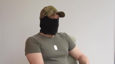 Askeri üniformalı ve şapkalı bir adamın portresi siyah bir kar maskesi takıyor ve gizli bir yüz ve yan gözle sorgulanıyor..