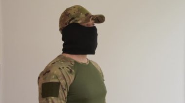 Kamuflaj üniformalı ve şapkalı siyah kar maskesi giymiş bir adamın portresi ve gizli bir yüz, yan görüş ile röportaj veriyor..