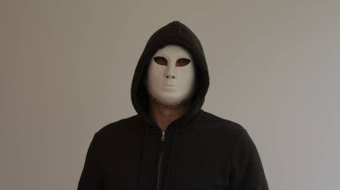 Beyaz bir maske takan bir adam portresi ve beyaz arka planda siyah kapüşonlu bir bornoz..