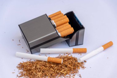 Sigaranın yanında sigara tabakası dağınık tütün ve beyaz arka planda boş sigara kovanları, ev yapımı sigara üretimi.