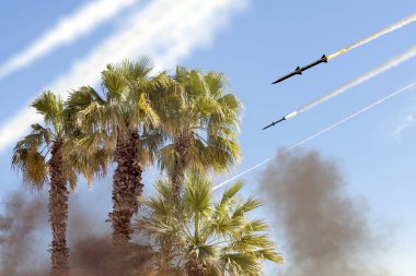 Palmiye ağaçlarının arkasında gökyüzünde balistik füzeler, füze fırlatma izleri. Kavram: İran ve İsrail arasındaki savaş, füze saldırısı.