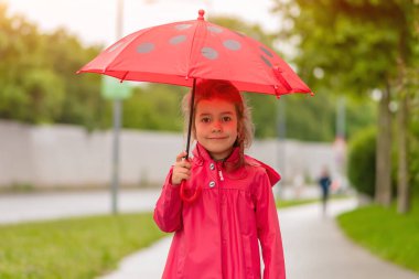Yağmurlu bir günde elinde kırmızı şemsiye tutan 6 yaşındaki bir kızın portresi..