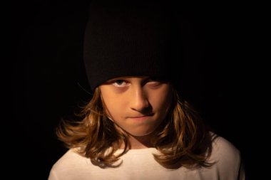 Siyah şapkalı, uzun sarı saçlı, koyu bir geçmişi olan bir genç. Doğrudan kameraya bakıyor, somurtkan, ciddi bir bakış..