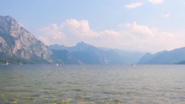 Arka planda Avusturya Alpleri ve evler ve dalgalarla Traunsee Gölü manzarası.