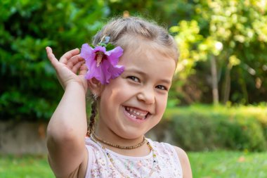 Gülen 6 yaşındaki bir kızın portresi. Saçında çiçekle çiçek açan bir bahçenin arka planında. Kızın süt dişleri dökülmüş..