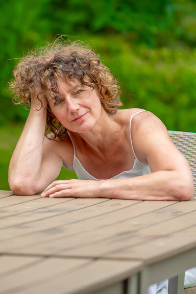 portrait of a romantic elderly woman 50-55 years old with curly hair at a table on the background of a summer garden