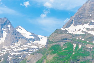 parlak yeşil yamaçları ve parlak mavi gökyüzünün altında karla kaplı tepeleri olan Avusturya manzarası. 