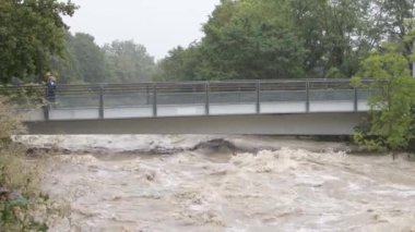 Şiddetli yağmurların ardından sel baskınları sırasında bir şehir nehri, yaya köprüsü altında fırtınalı akarsular.