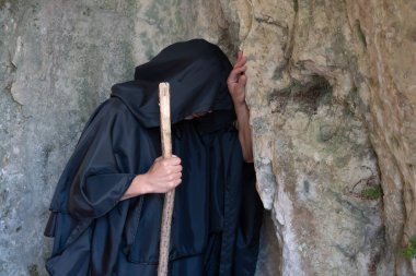 Siyah cüppeli bir keşiş asasını taşırken kafasını bir kayaya yasladı..