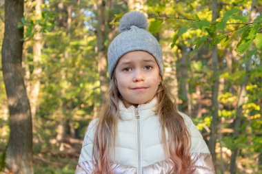 Güneşli bir günde, sonbahar ormanında şapkalı ve ceketli küçük bir kızın portresi..