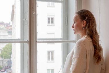 Öğleden sonra şehir caddesine bakan büyük bir pencerede kazak giymiş güzel bir kadın huzur ve düşüncenin tadını çıkarıyor..