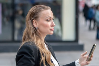 35-40 yaşlarındaki bir kadının portresi. Elinde akıllı bir telefonla Avrupa 'nın bir kentsel caddesinin bulanık arka planında..