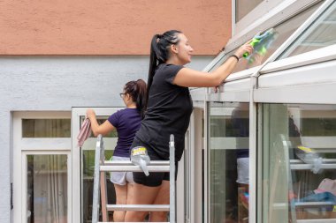 Bir evin terasında pencereleri temizleyen iki kadın.